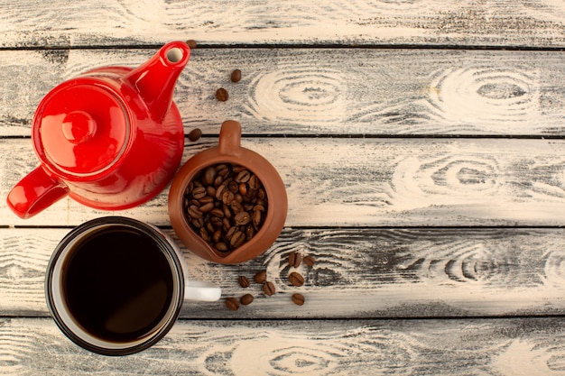 Un bollitore rosso con vista dall'alto con una tazza di caffè e semi di caffè marroni sullo scrittorio rustico grigio beve il colore del caffè