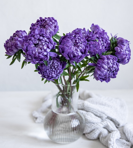 Un bouquet di crisantemi blu in un vaso di vetro e un elemento a maglia su uno sfondo bianco.