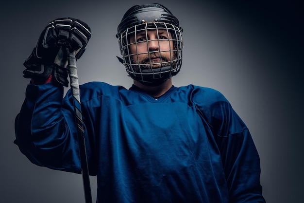Un brutale giocatore di hockey su ghiaccio con la barba in casco di sicurezza tiene il bastone da gioco su uno sfondo grigio vignetta.