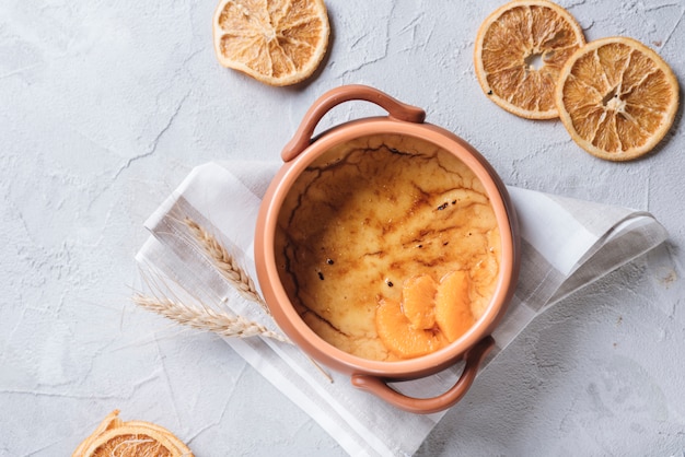 Un budino di crema pasticcera arancia con fette di frutta secca su sfondo bianco cemento