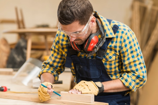 Un carpentiere maschio che fa marcatura sul blocco di legno con la matita