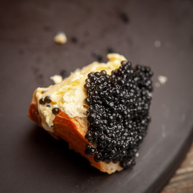 Un certo caviale nero con burro su pane su fondo scuro, vista dell'angolo alto.