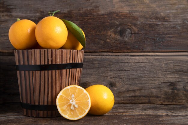 Un cesto di legno pieno di frutta fresca di limone con foglie poste su un tavolo di legno. Foto di alta qualità