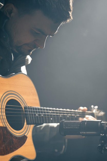 Un chitarrista suona una chitarra acustica con un microfono su uno sfondo scuro