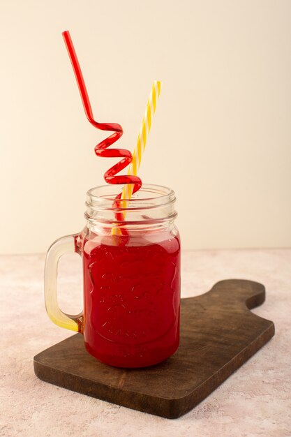 Un cocktail rosso ciliegia con vista frontale con cannucce all'interno di una lattina fresca di raffreddamento sulla scrivania in legno e rosa