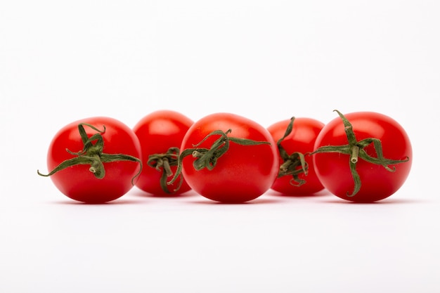 Un colpo del primo piano di cinque pomodori ciliegia su una parete bianca - perfetto per un blog dell'alimento