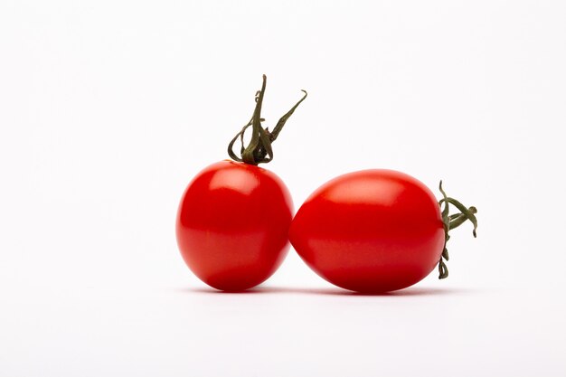 Un colpo del primo piano di due pomodori ciliegia su una priorità bassa bianca - perfetto per un blog dell'alimento
