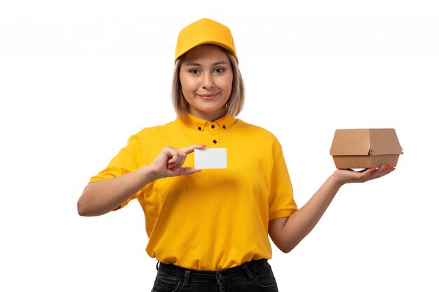 Un corriere femminile di vista frontale in camicia gialla che tiene la scatola della tenuta del cappuccio e la carta bianca che sorridono sul bianco