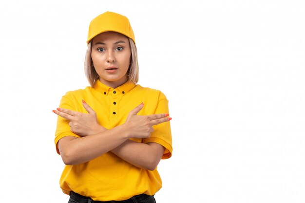 Un corriere femminile di vista frontale in camicia gialla del berretto giallo e jeans neri che posano sul servizio bianco della ragazza di consegna del fondo