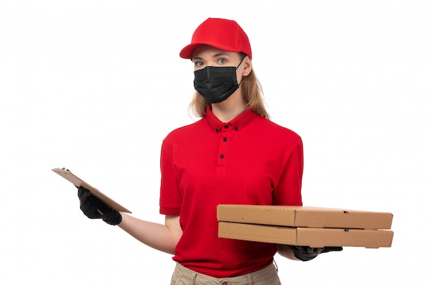 Un corriere femminile di vista frontale in guanti rossi della camicia rossa della camicia rossa e scatole nere della pizza della tenuta della maschera su bianco