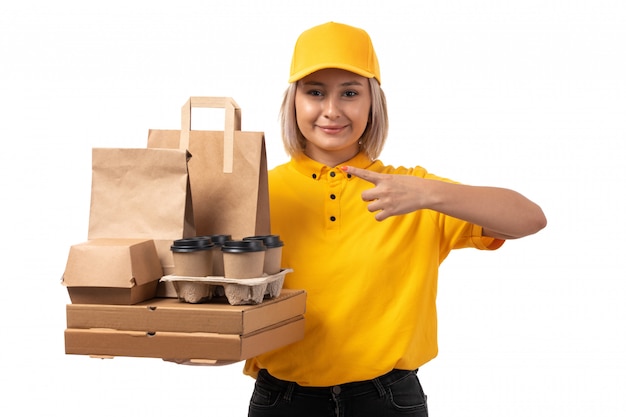 Un corriere femminile di vista frontale in protezione gialla della camicia gialla e jeans neri che tengono i contenitori di pizza e le tazze di caffè che sorridono sul bianco