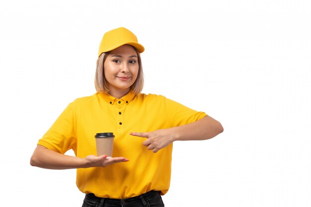Un corriere femminile di vista frontale in protezione gialla della camicia gialla e jeans neri che tengono la tazza di caffè che sorride sul bianco