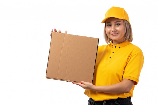Un corriere femminile di vista frontale in scatola gialla che tiene la scatola della tenuta del cappuccio giallo che sorride sul bianco