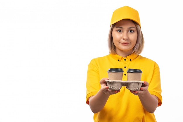 Un corriere femminile di vista frontale in tazza gialla che sorride tenendo le tazze di caffè sorridenti della tenuta su bianco