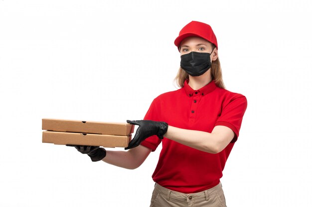 Un corriere femminile vista frontale in camicia rossa berretto rosso guanti neri e maschera nera pantaloni marroni che tengono scatole per pizza