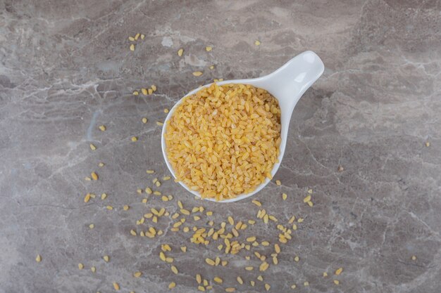 Un cucchiaio di bulgur e bulgur sparsi sulla superficie del marmo