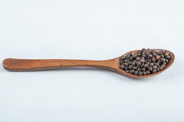 Un cucchiaio di legno pieno di pepe secco su sfondo bianco.