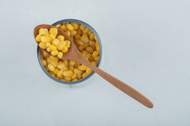 Un cucchiaio di legno pieno di semi di popcorn su bianco.