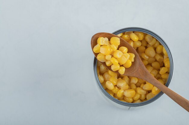 Un cucchiaio di legno pieno di semi di popcorn su bianco.
