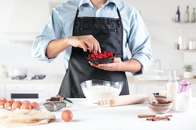 Un cuoco in una cucina rustica. Il maschio passa con ingredienti per cucinare prodotti a base di farina o pasta, pane, muffin, torte, torte, pizza