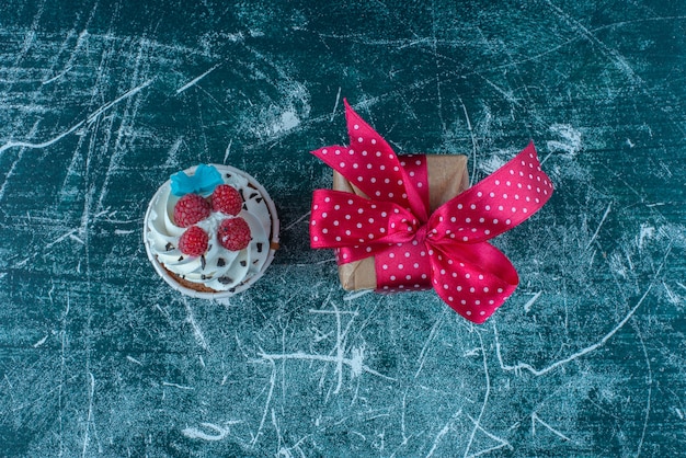 Un cupcake e una piccola confezione regalo su sfondo blu. Foto di alta qualità