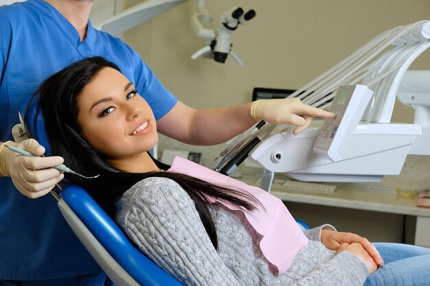 Un dentista passa al lavoro su una giovane donna paziente con strumenti dentali.