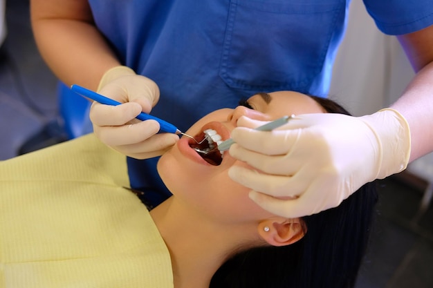 Un dentista passa al lavoro su una giovane donna paziente con strumenti dentali.