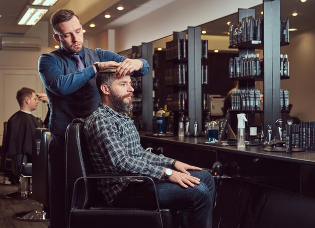 Un elegante maestro barbiere fa un taglio di capelli al cliente. Taglio di capelli da uomo in un barbiere. Acconciare i capelli con un pettine.