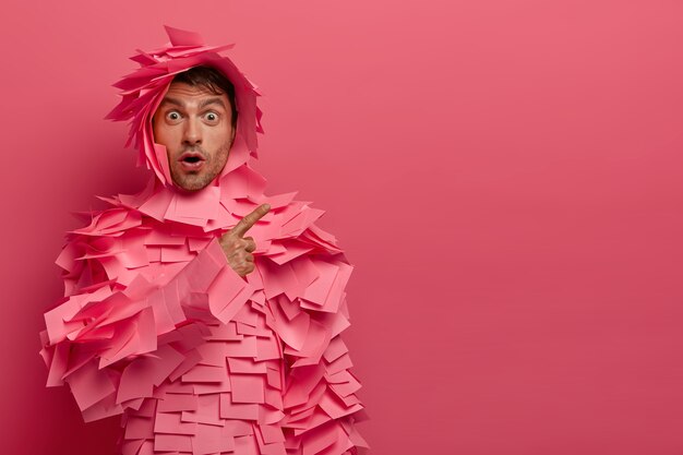 Un europeo imbarazzato e impressionato ascolta notizie scioccanti, indossa costumi di carta, indica uno spazio vuoto, resta senza parole, isolato su un muro rosa, pubblicizza oggetti, sussulta di meraviglia.