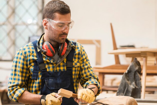 Un falegname maschio che scolpisce la forma di legno con lo scalpello nell&#39;officina