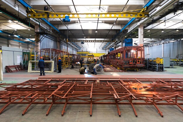 Un giorno lavorativo di moderna produzione di auto filobus per autobus automatici con auto non finite lavoratori in uniforme protettiva in background di fabbrica braccio di saldatura della linea di assemblaggio di automobili