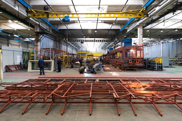 Un giorno lavorativo di moderna produzione di auto filobus per autobus automatici con auto non finite lavoratori in uniforme protettiva in background di fabbrica braccio di saldatura della linea di assemblaggio di automobili