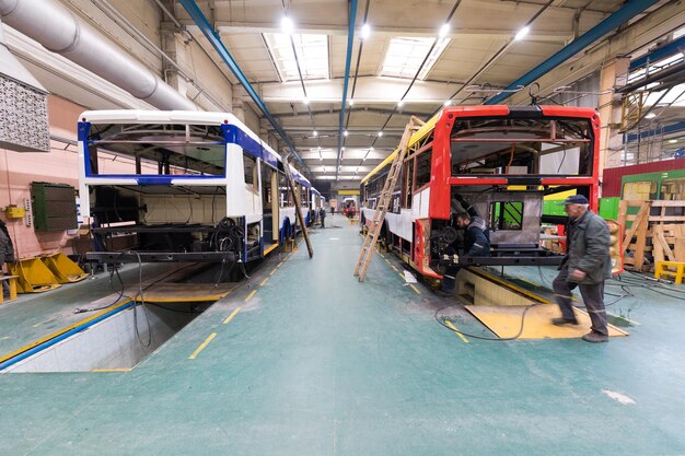 Un giorno lavorativo di moderna produzione di autobus automatici con lavoratori di automobili non finiti in uno sfondo di parti automobilistiche uniformi protettive