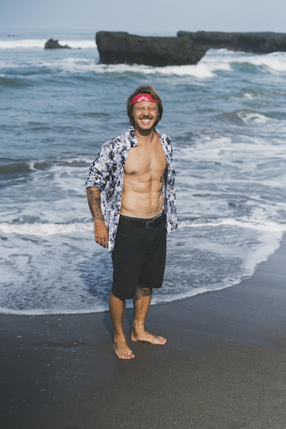 Un giovane bell'uomo con una bandana rossa cammina lungo l'oceano in spiaggia.