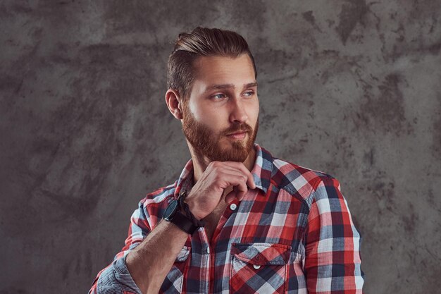 Un giovane bell'uomo modello dai capelli rossi in una camicia di flanella su sfondo grigio.