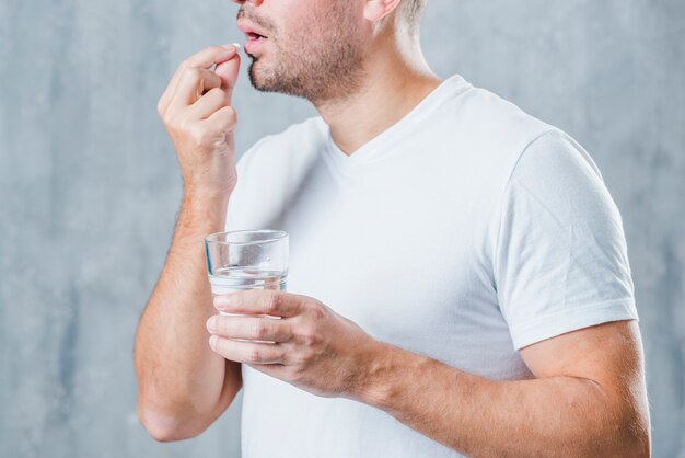 Un giovane che tiene bicchiere d&#39;acqua che prende medicina