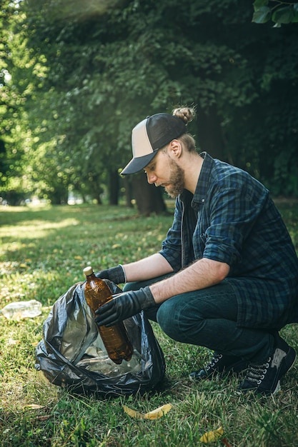 Un giovane con un sacco della spazzatura nella foresta pulisce le bottiglie di plastica