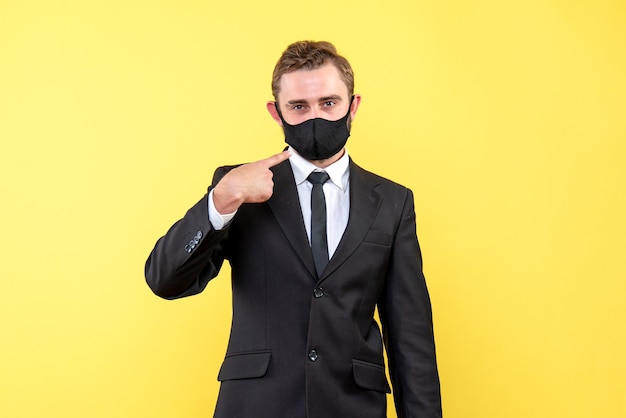 Un giovane con una maschera facciale che mostra e spiega che è obbligatorio indossare una maschera per prevenire l'infezione da coronavirus su giallo