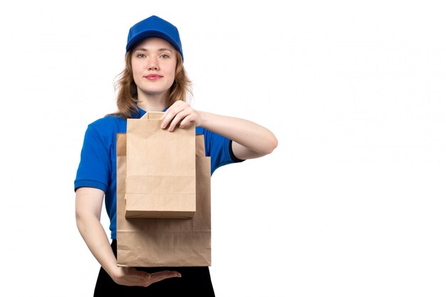Un giovane corriere femminile di vista frontale in cappuccio blu della camicia blu e pantaloni neri che tengono i pacchetti dell'alimento di consegna su bianco