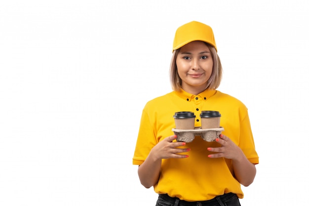 Un giovane corriere femminile di vista frontale in cappuccio giallo della camicia gialla e jeans neri che tengono le tazze di caffè che sorridono
