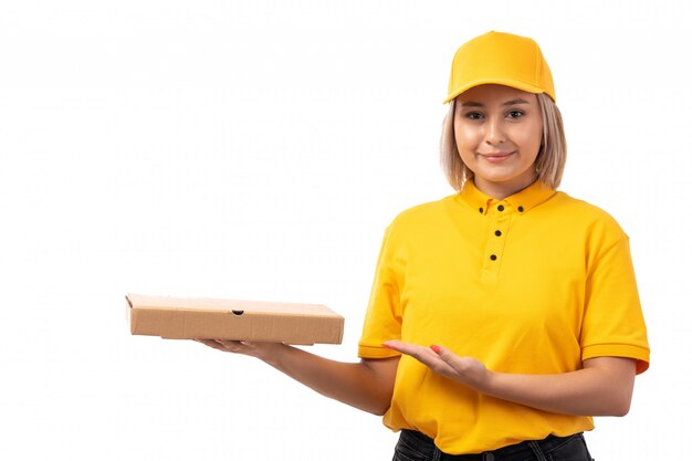 Un giovane corriere femminile di vista frontale in cappuccio giallo della camicia gialla e jeans neri che tengono sorridere del contenitore di pizza