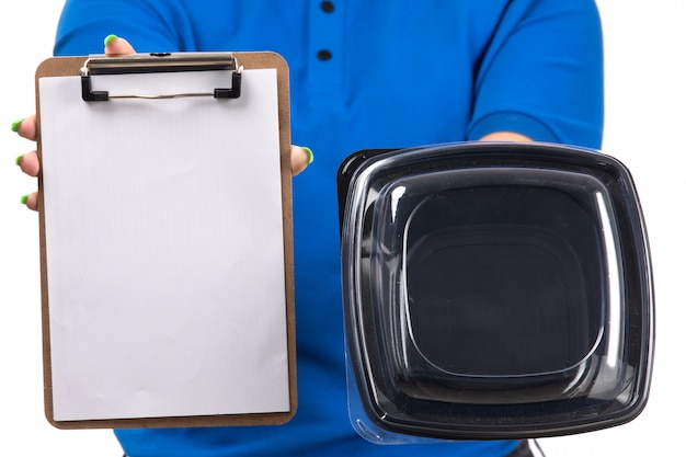 Un giovane corriere femminile di vista frontale in ciotola e blocco note blu di consegna dell'alimento della tenuta dell'uniforme per le firme