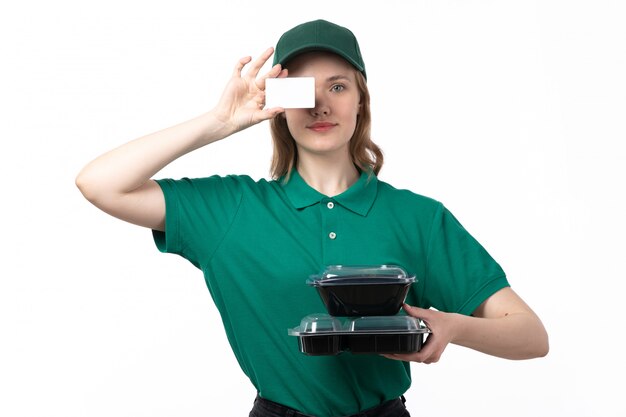 Un giovane corriere femminile di vista frontale in ciotole verdi della tenuta dell'uniforme con la carta bianca dell'alimento e sorridere sul bianco