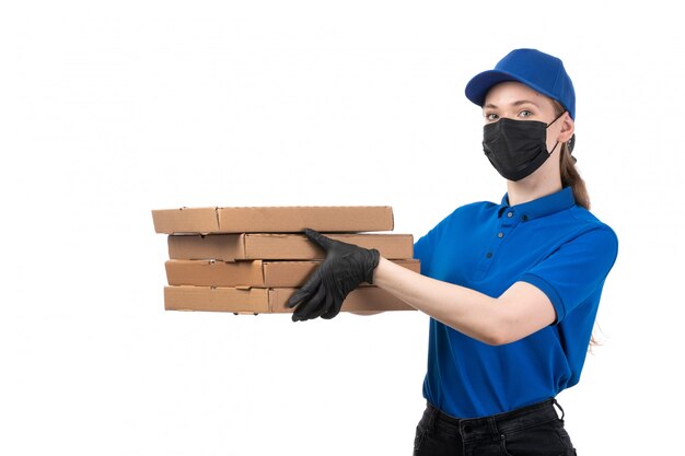 Un giovane corriere femminile di vista frontale in guanti neri uniformi blu e maschera nera che tiene i pacchetti di consegna dell'alimento