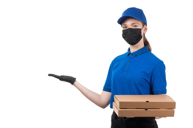 Un giovane corriere femminile di vista frontale in guanti neri uniformi blu e maschera nera che tiene i pacchetti di consegna dell'alimento