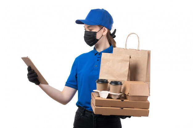 Un giovane corriere femminile di vista frontale in guanti neri uniformi blu e maschera nera che tiene i pacchetti e il blocco note di consegna dell'alimento
