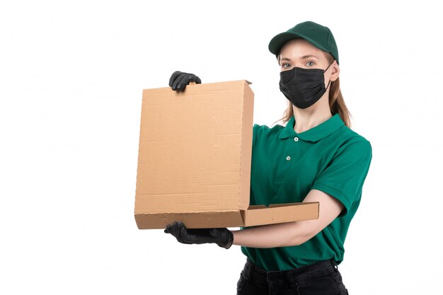 Un giovane corriere femminile di vista frontale in guanti neri uniformi verdi e maschera nera che tiene consegna del pacchetto di consegna dell'alimento
