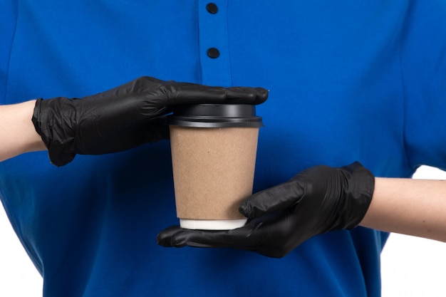 Un giovane corriere femminile di vista frontale in maschera nera uniforme blu e guanti che tengono tazza di caffè