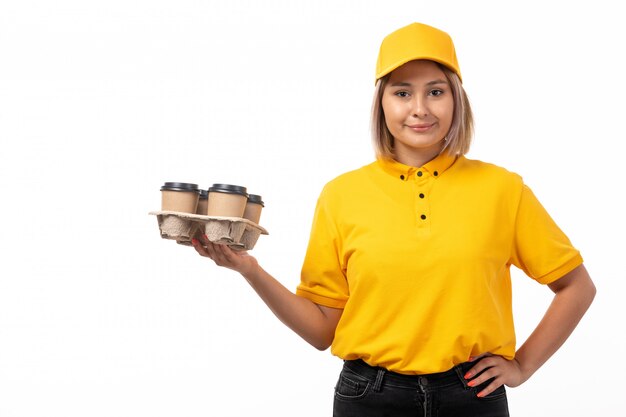 Un giovane corriere femminile di vista frontale in protezione gialla del yellwo della camicia e jeans neri che tengono le tazze di caffè che sorridono