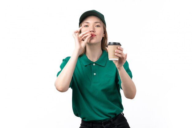 Un giovane corriere femminile di vista frontale in tazza di caffè verde della tenuta dell'uniforme che posa sul bianco